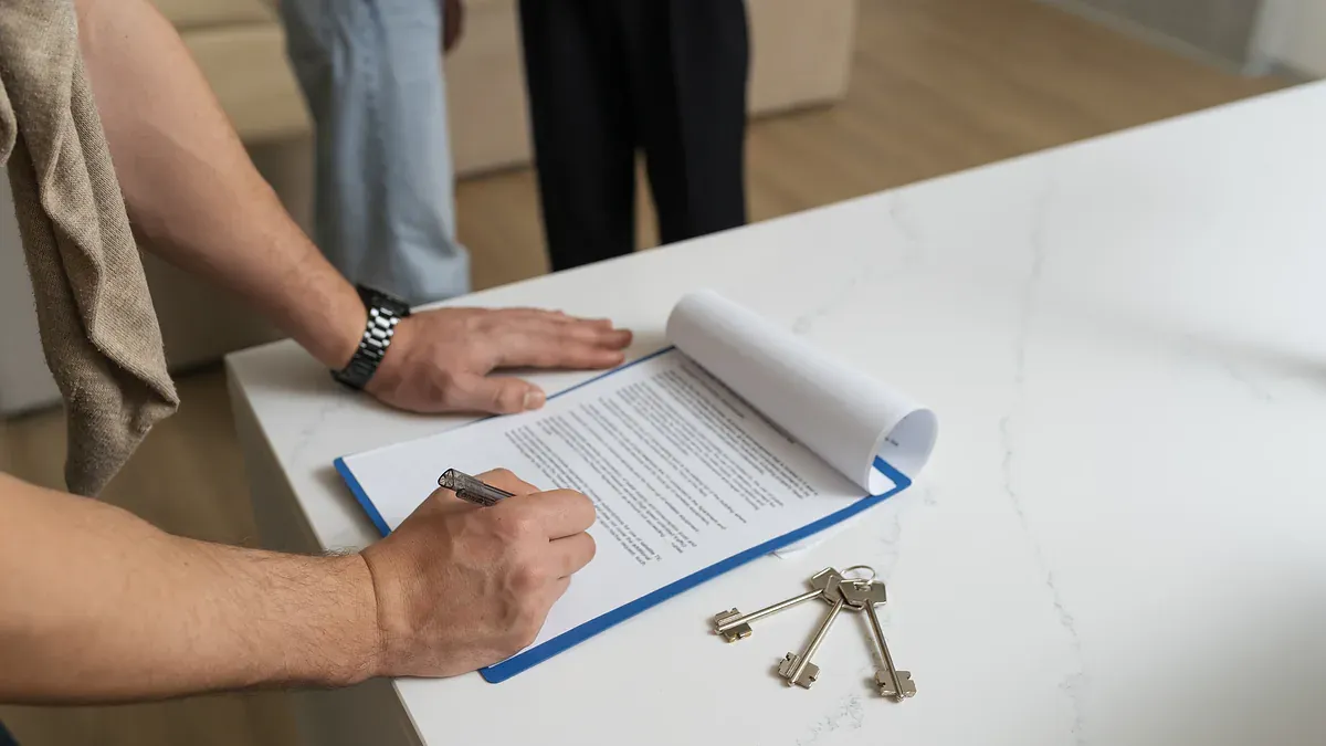 Покупець підписує договір купівлі-продажу квартири поряд із ключами на світлому столі